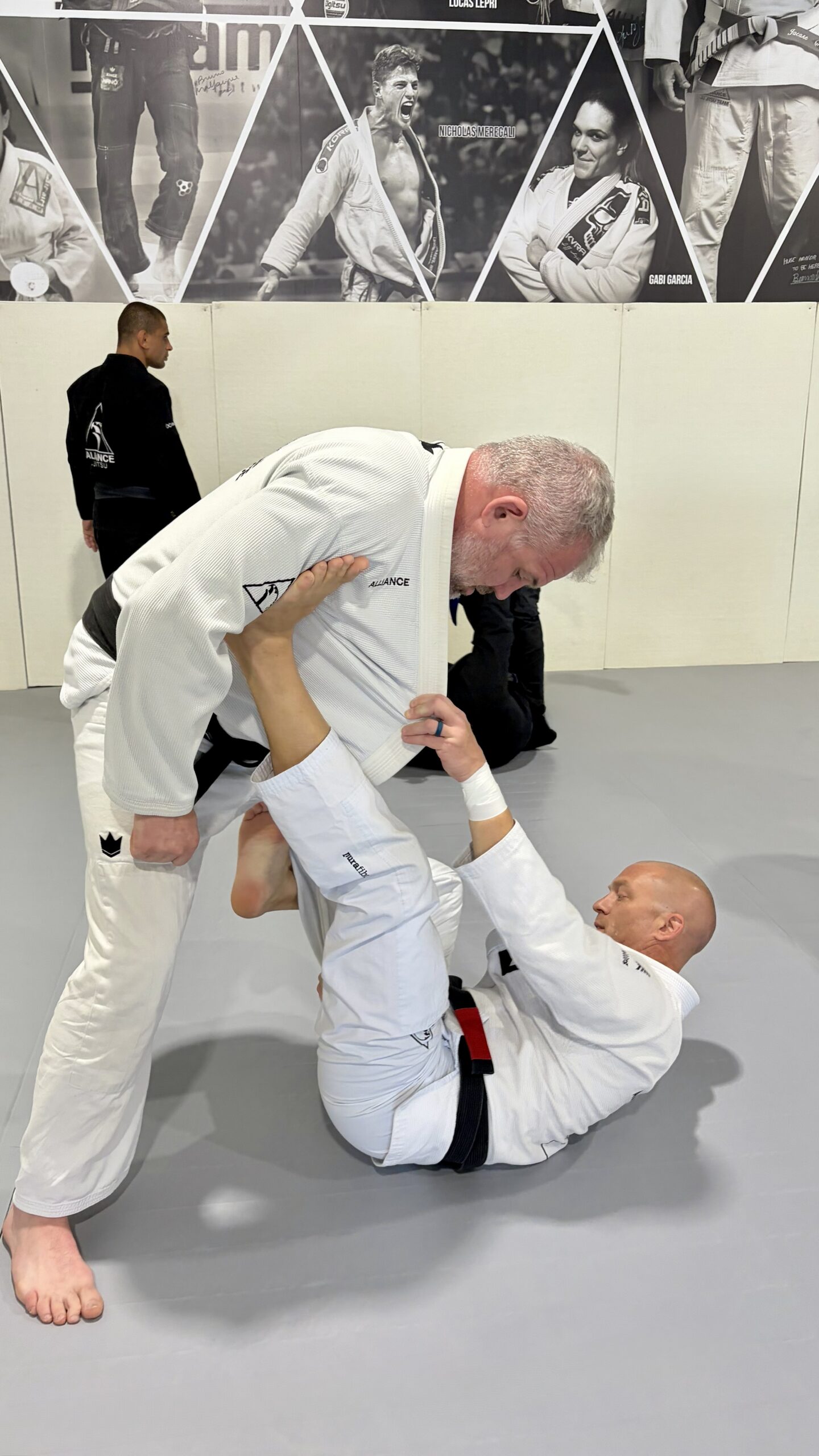 White-haired man in a white gi grapples a partner during open mat