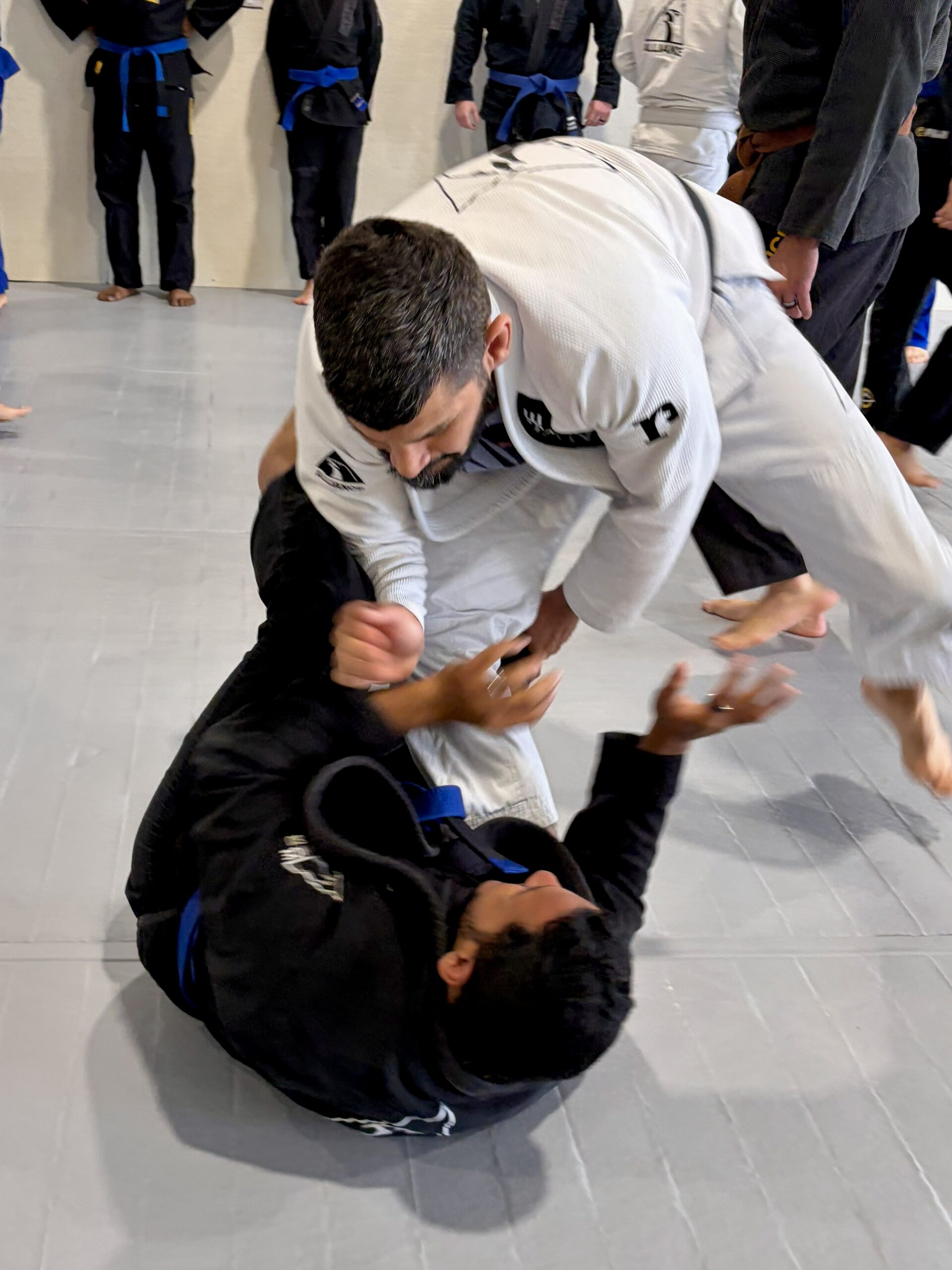 Man in a white gi drives a takedown on a partner during rounds
