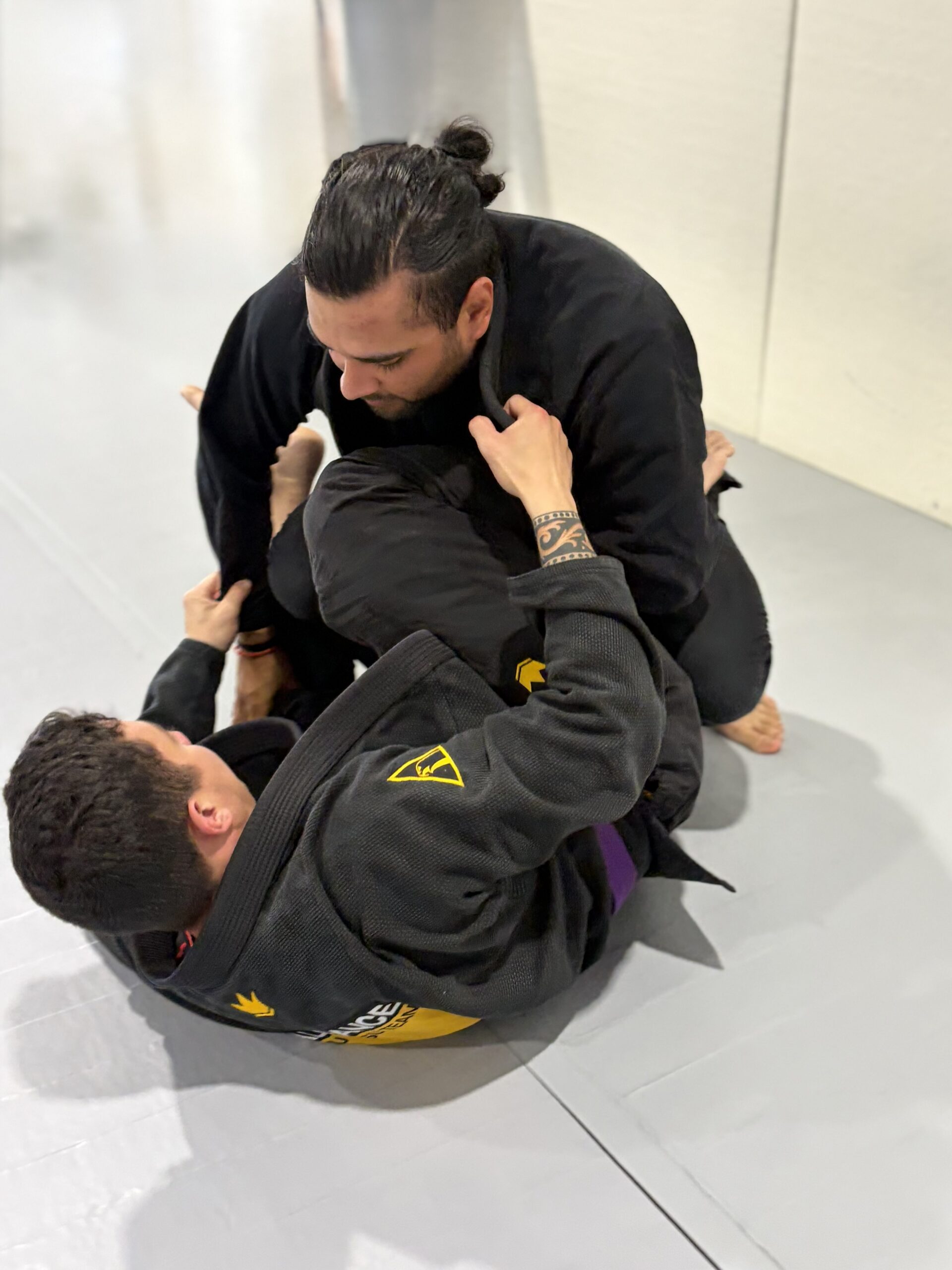 Grappler in a black gi works from closed guard against a partner with a purple belt