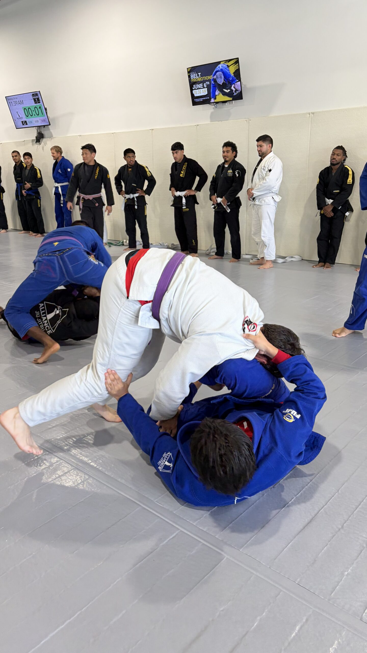 Man in a white gi and purple belt drills standing guard passing against a partner