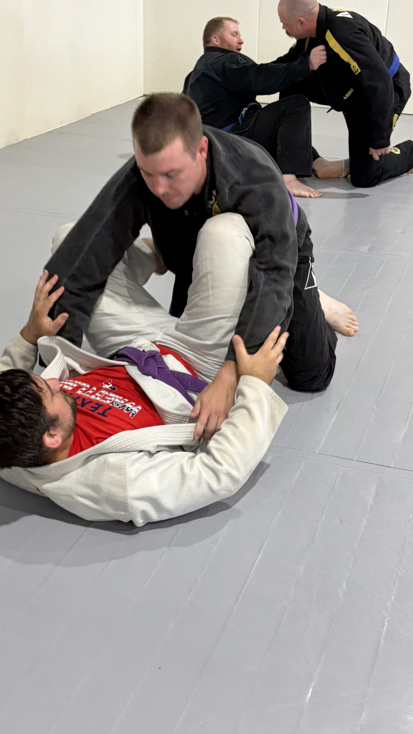 Purple belt in a black gi controls a partner pinned on the mat