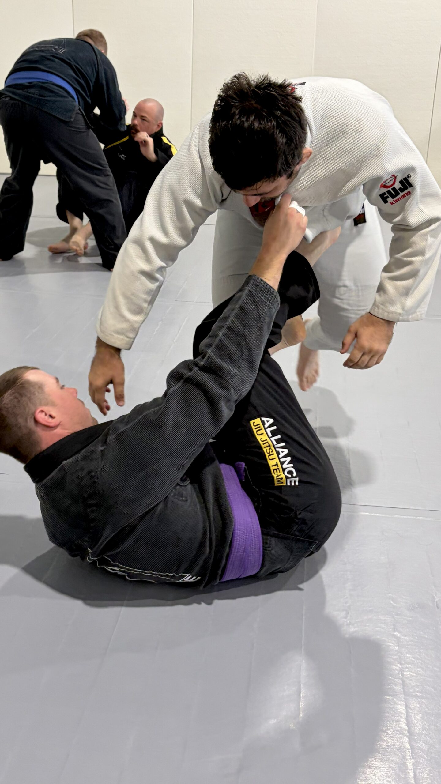 Young grappler passes the guard of a partner in a black gi wearing a purple belt