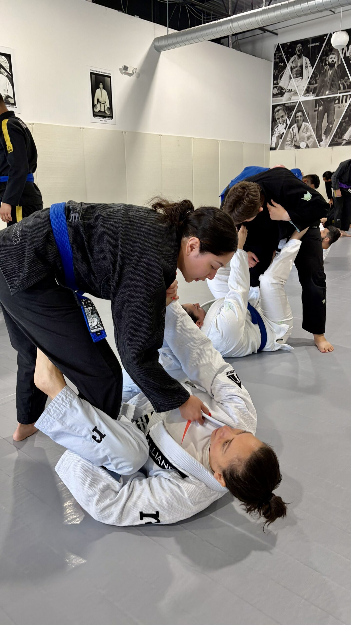 Woman in a black gi plays open guard against a partner in white