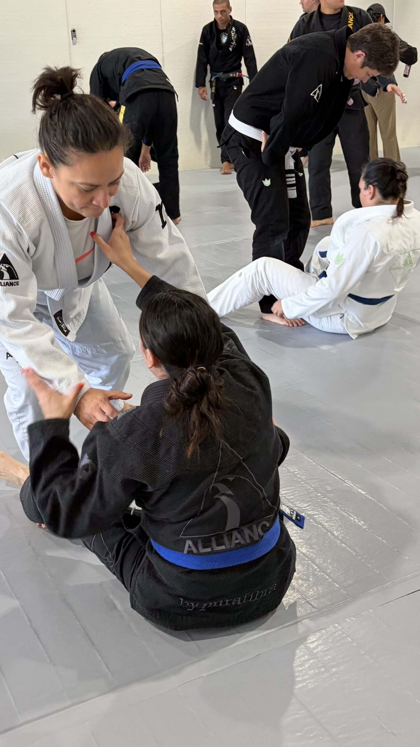 Two women in white and black gis drill from the knees during adult open mat