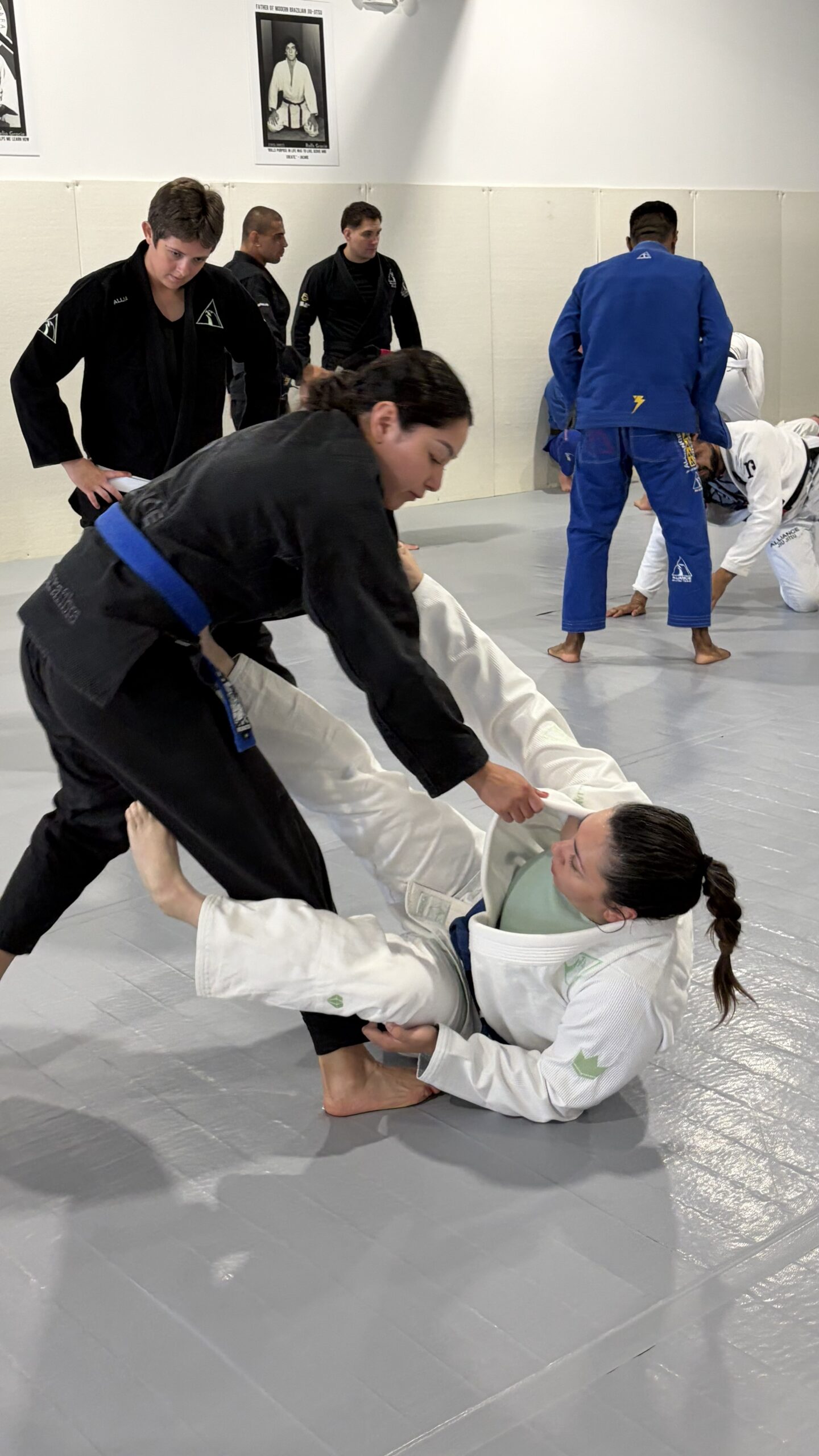 Woman in a black gi works a partner's guard during open mat