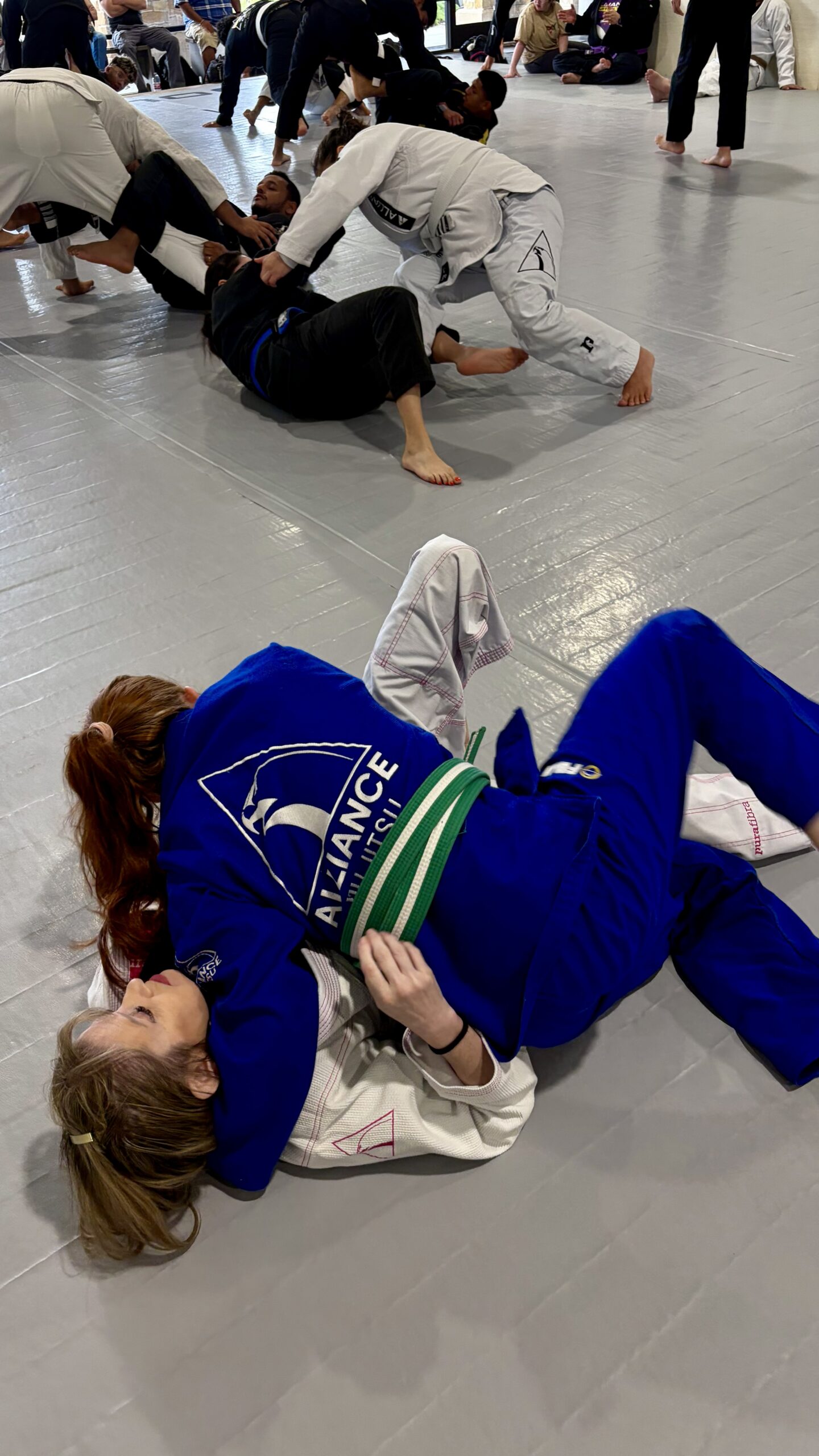 Two young women grapple on the mat, one in a blue gi on top of one in white