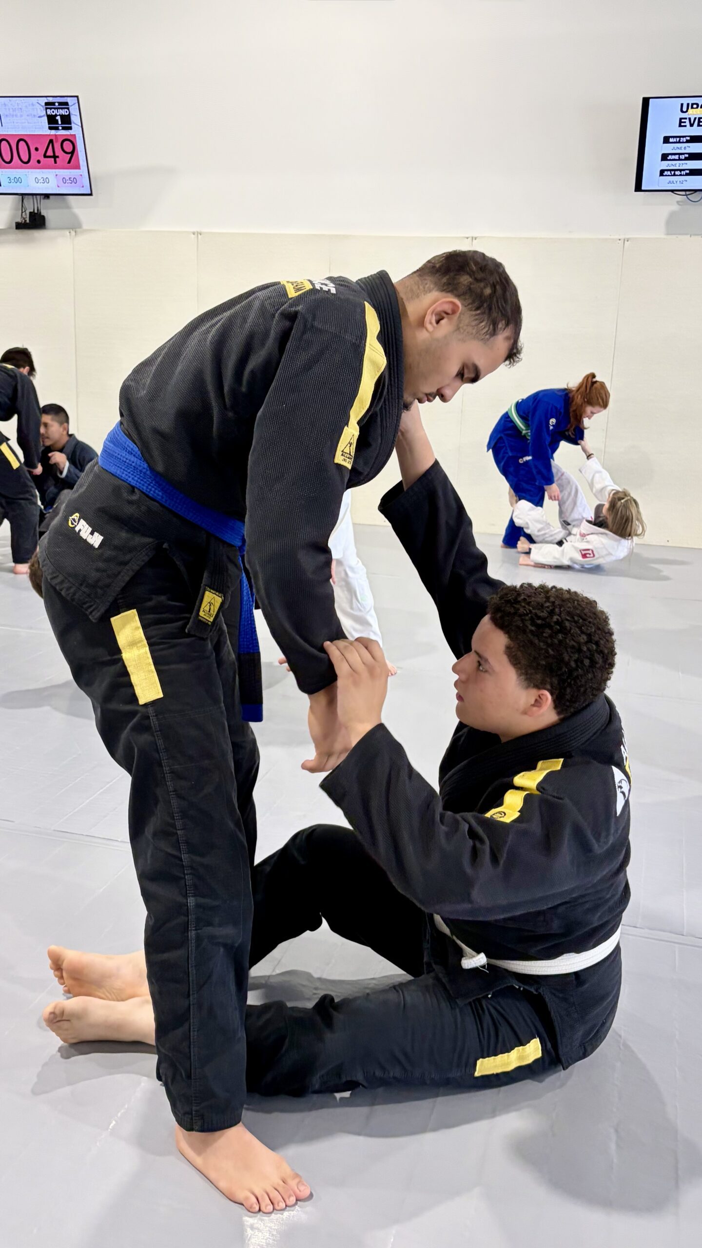 Teen in a black gi grips a younger partner during a timed round