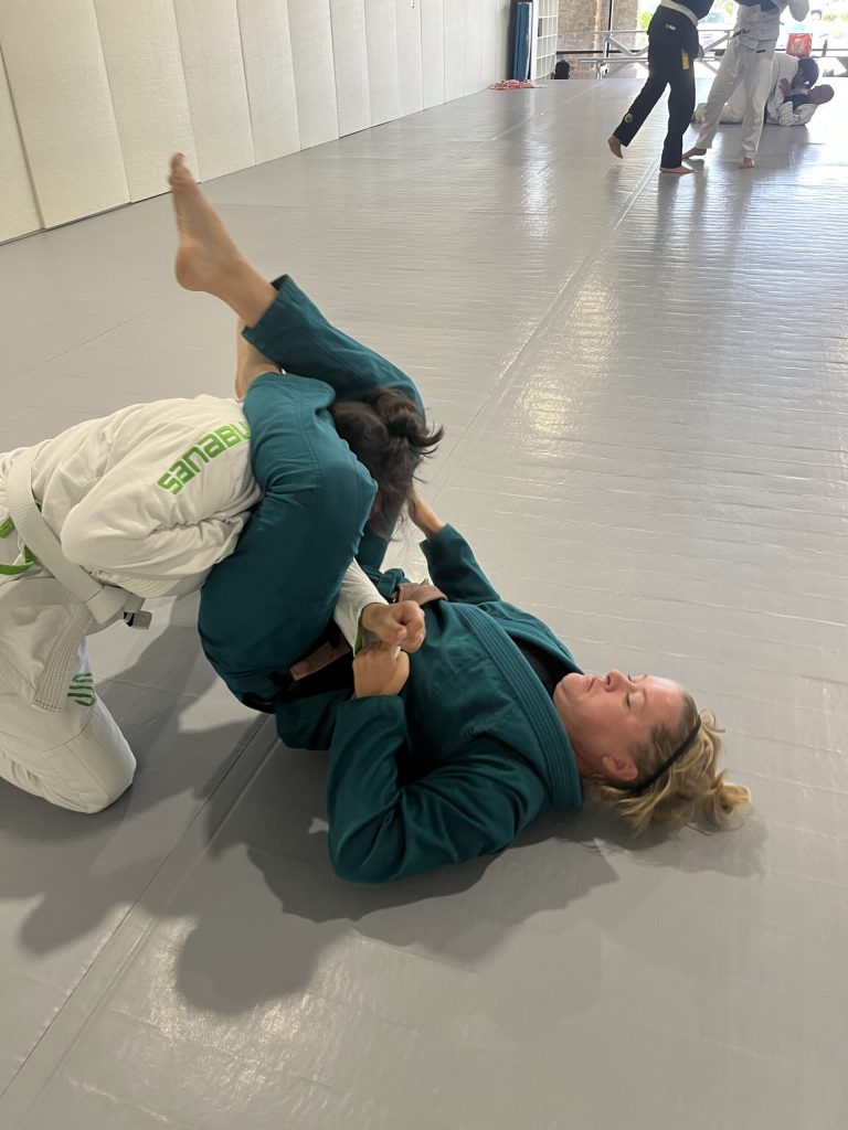 Brown belt woman plays guard against a white belt during self-defense seminar training