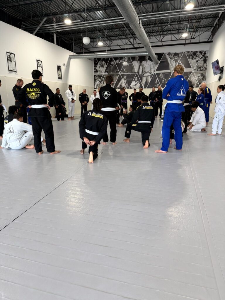 Adult class kneels on the mats as an instructor explains the drill