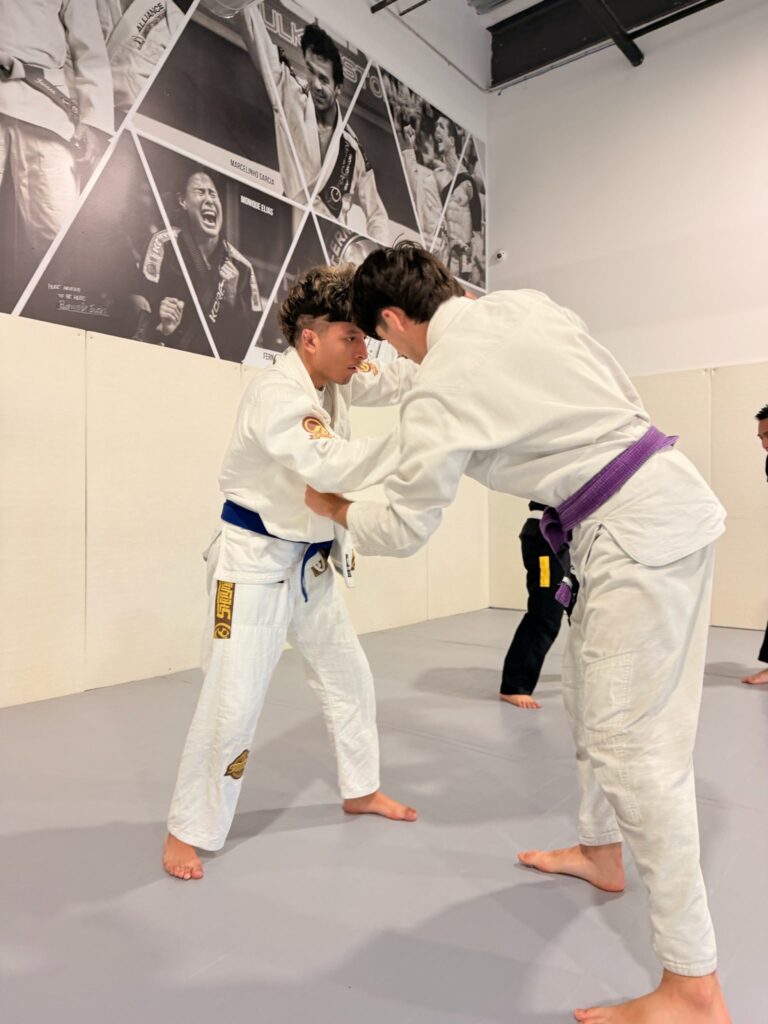 Two students in white gis grip fighting from standing during sparring