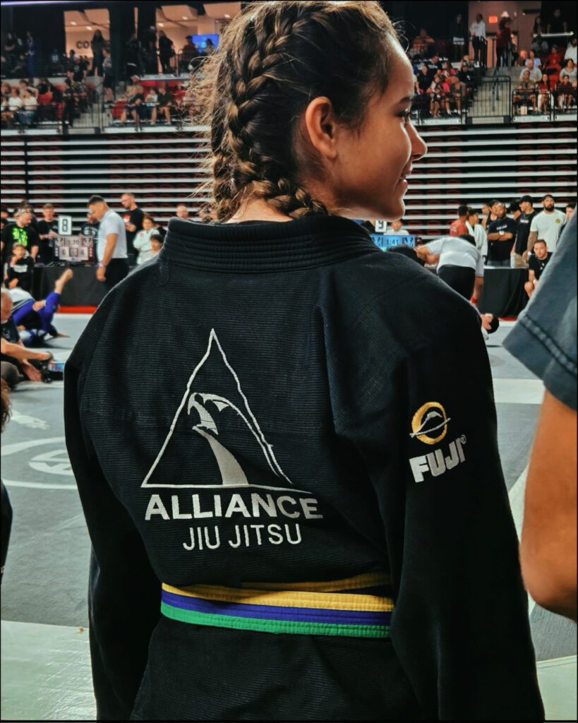 Realyn Oehlert waits mat-side with the team logo across the back of her gi