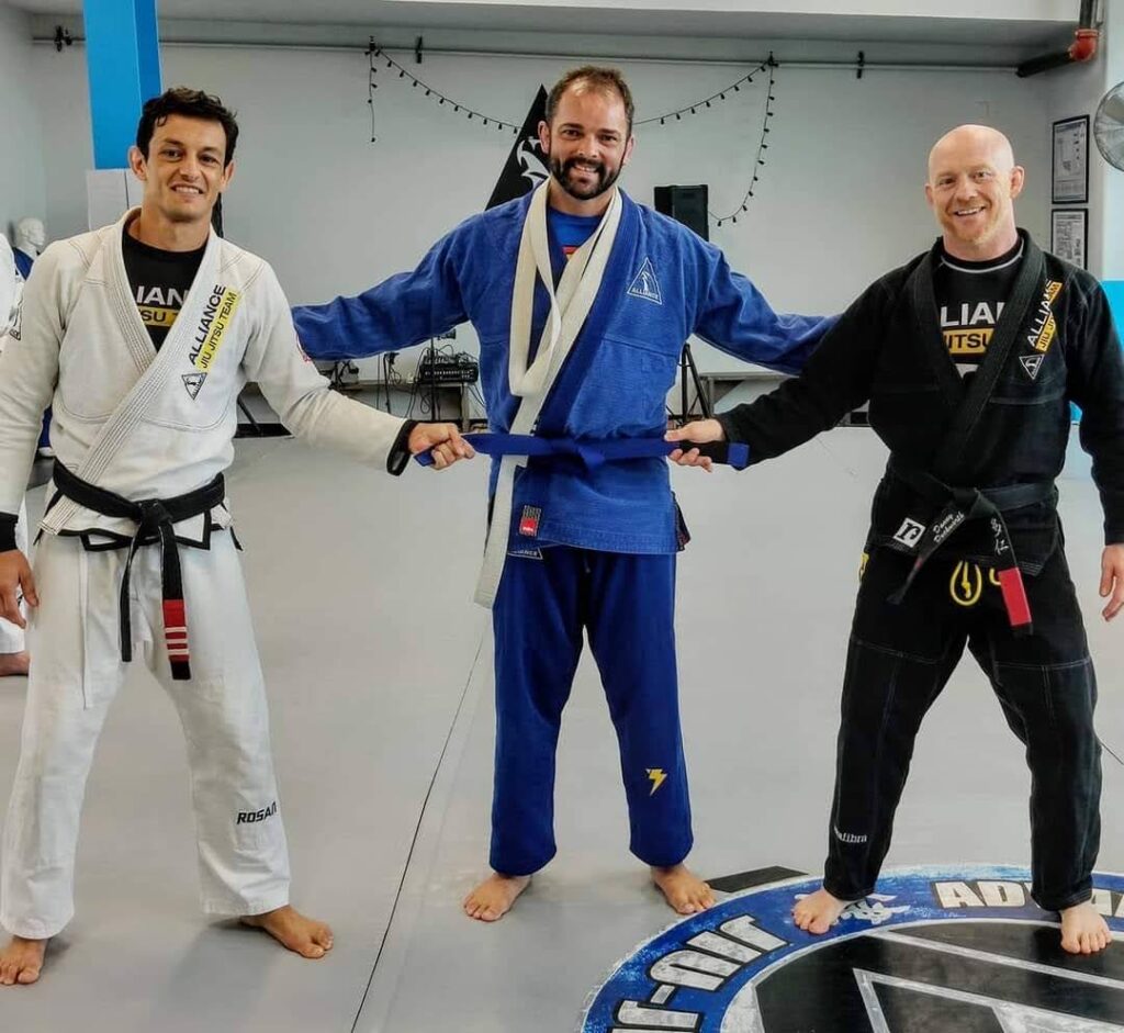 Two black belts tie a blue belt around Jeremy Woodin’s waist